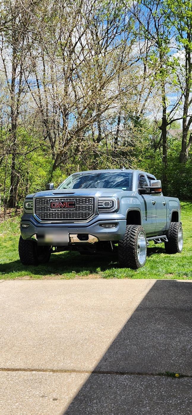 A lifted gray GMC pickup parked on grass